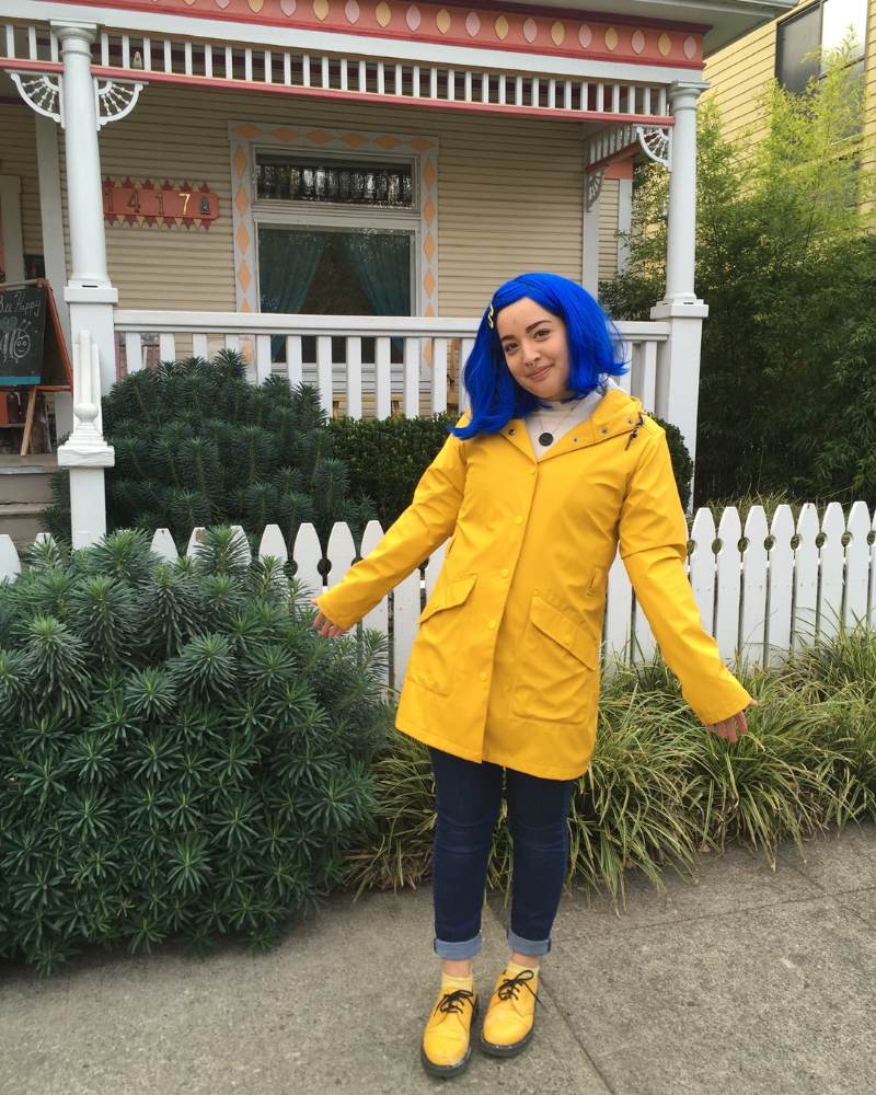 Buffalo Employee dressed in yellow raincoat with blue hair standing outside of a victorian house.