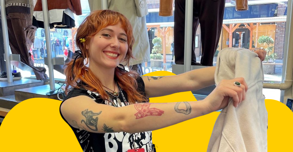 Buffalo Exchange employee holding up an article of clothing with a yellow backdrop