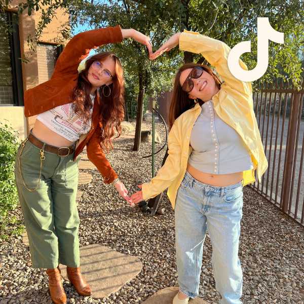 Two employees in trendy, contemporary fall outfits posing with their arms forming the shape of a heart, with TikTok logo overlay Two employees in trendy, contemporary fall outfits posing with their arms forming the shape of a heart, with TikTok logo overlay